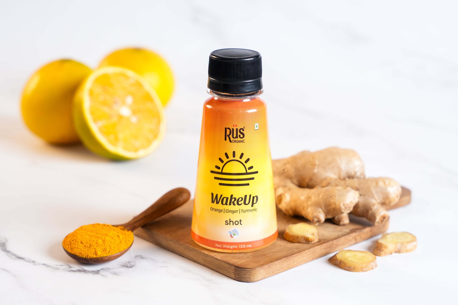 A vibrant 125ml bottle of Rus Organic's "WakeUp" shot is displayed on a wooden board surrounded by fresh ginger root, turmeric powder, and halved oranges. The orange-yellow gradient bottle features bold sunrise graphics, representing an energizing start to the day. Infused with orange, ginger, and turmeric, this wellness shot is designed to strengthen immunity, improve digestion, and support hydration with natural ingredients and antioxidants.