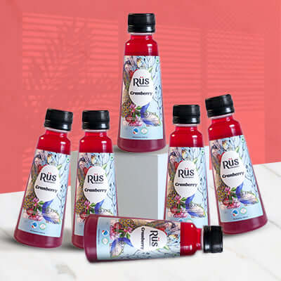 A single, clear plastic bottle filled with red Rus Organic Cranberry Juice. The bottle has a black cap and a colorful label featuring a peacock feather design, cranberries, blueberries, and the "Rūs Organic Cranberry" logo. The background is a solid gray