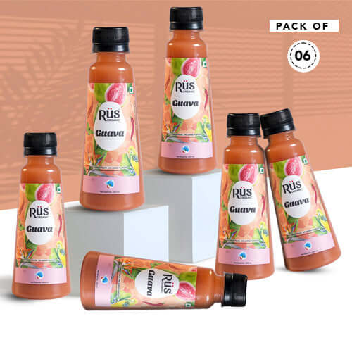 A product shot of Rus Organic Guava Nectar, emphasizing its natural and fresh qualities. The bottle is positioned amongst fresh guavas on a wet, vibrant pink background, suggesting a refreshing and organic drink.