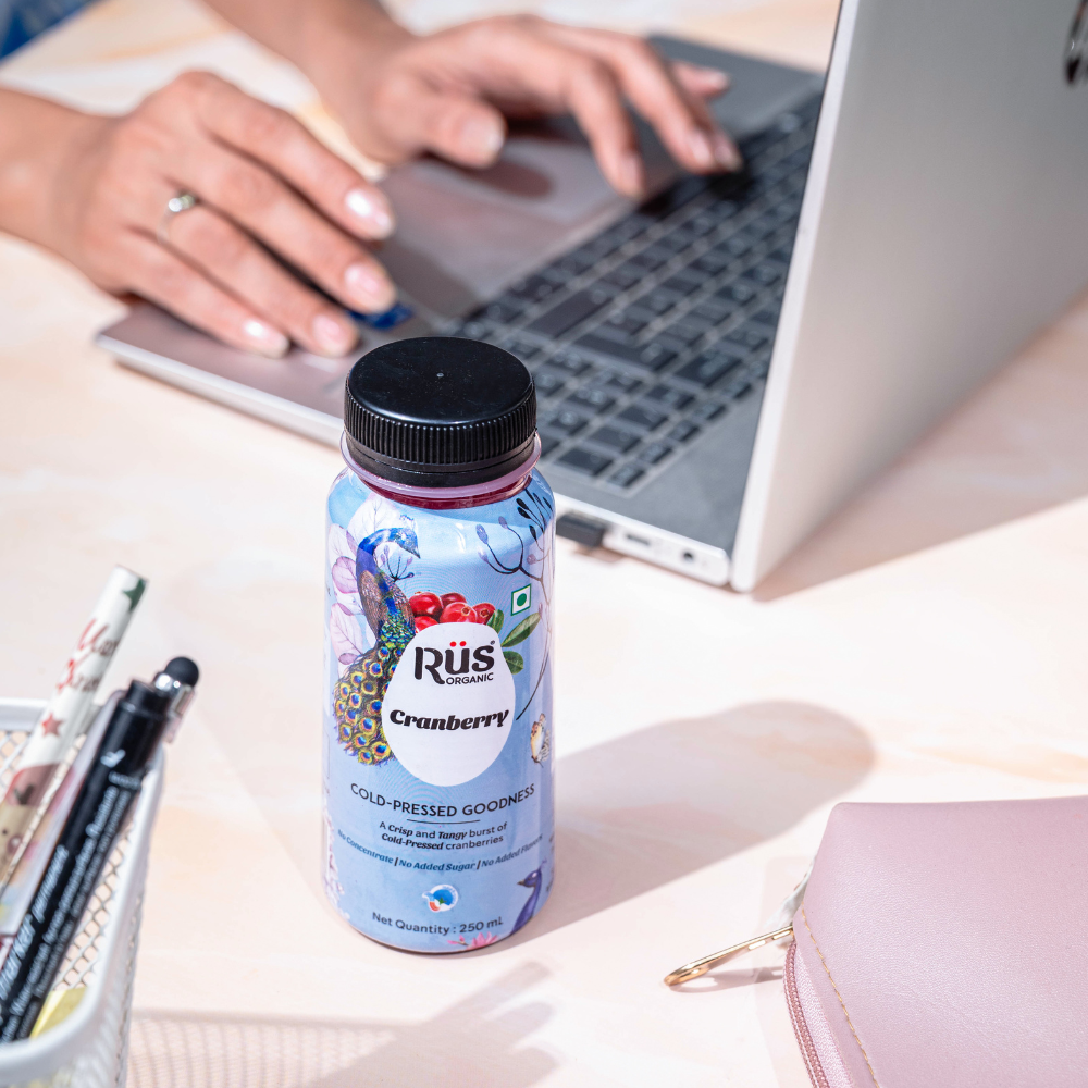 Organic cranberry juice of rus organic on the office desk of an employee who is working on laptop while enjoyinng cranberry juice