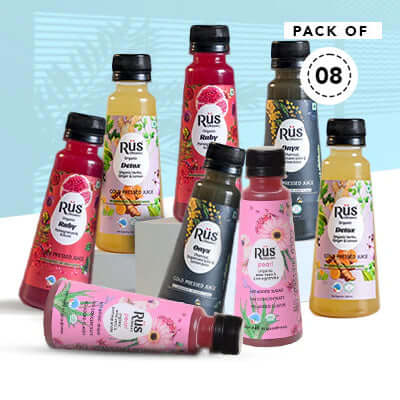 A pack of eight small, clear plastic bottles of Rus organic cold-pressed juices. The bottles have black caps and colorful labels indicating different flavors like ruby (pomegranate), onyx, and detox (turmeric, ginger, lemon). They are arranged on a light blue surface with a "PACK OF 08" sticker visible in the upper right corner.
