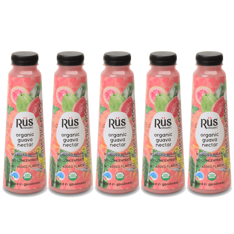 A product shot of Rus Organic Guava Nectar, emphasizing its natural and fresh qualities. The bottle is positioned amongst fresh guavas on a wet, vibrant pink background, suggesting a refreshing and organic drink.