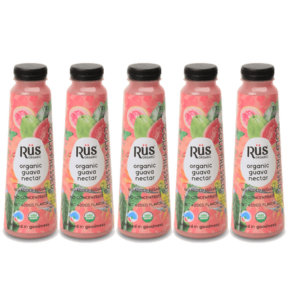 A product shot of Rus Organic Guava Nectar, emphasizing its natural and fresh qualities. The bottle is positioned amongst fresh guavas on a wet, vibrant pink background, suggesting a refreshing and organic drink.